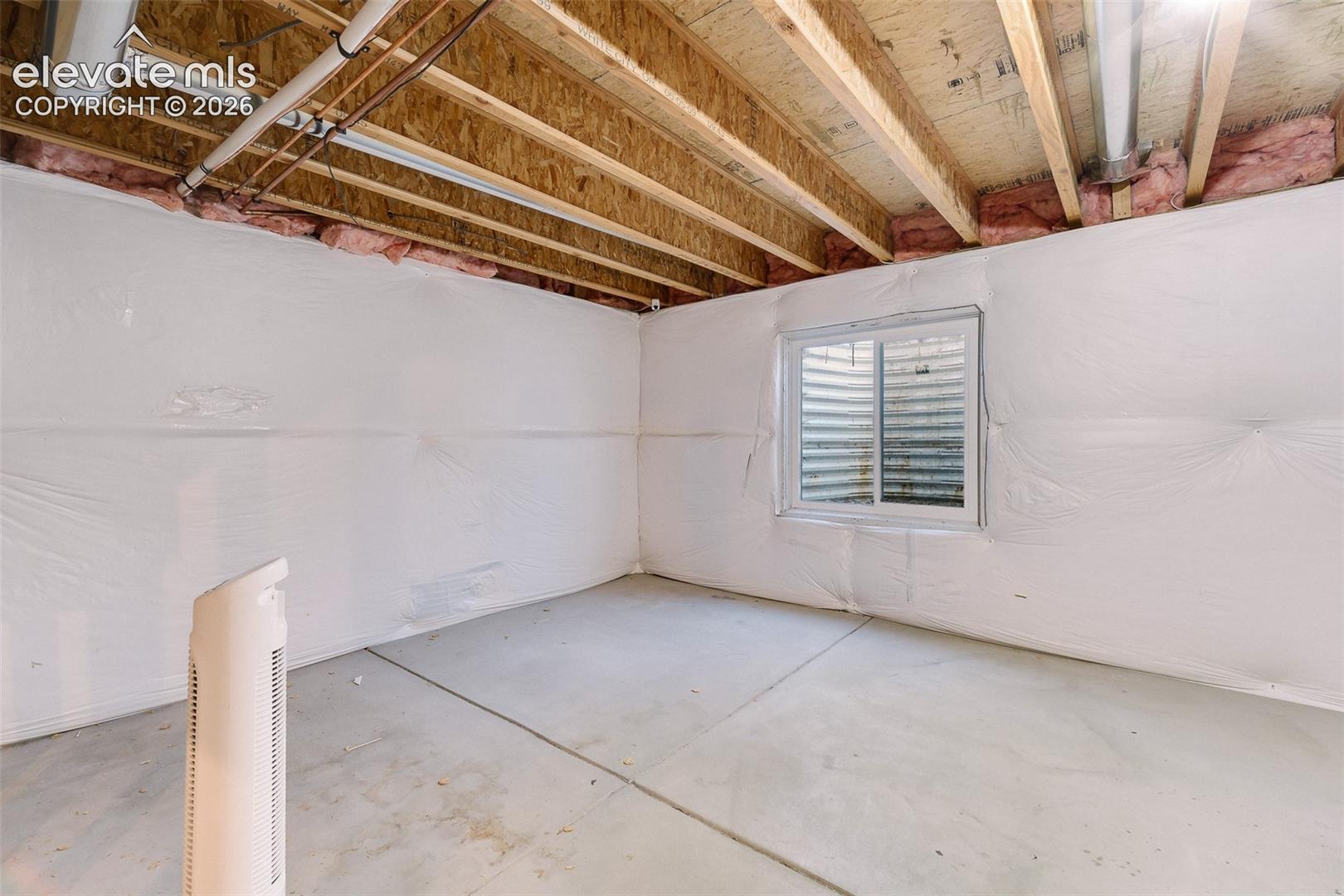 Unfinished lower level featuring concrete flooring, exposed wooden joists, wall insulation, and a single egress window