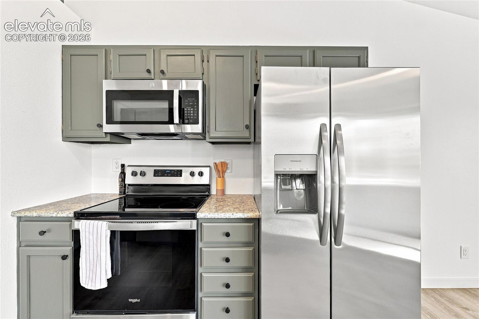 Kitchen featuring stainless steel appliances, grey cabinetry, light-colored countertops, and a side-by-side refrigerator