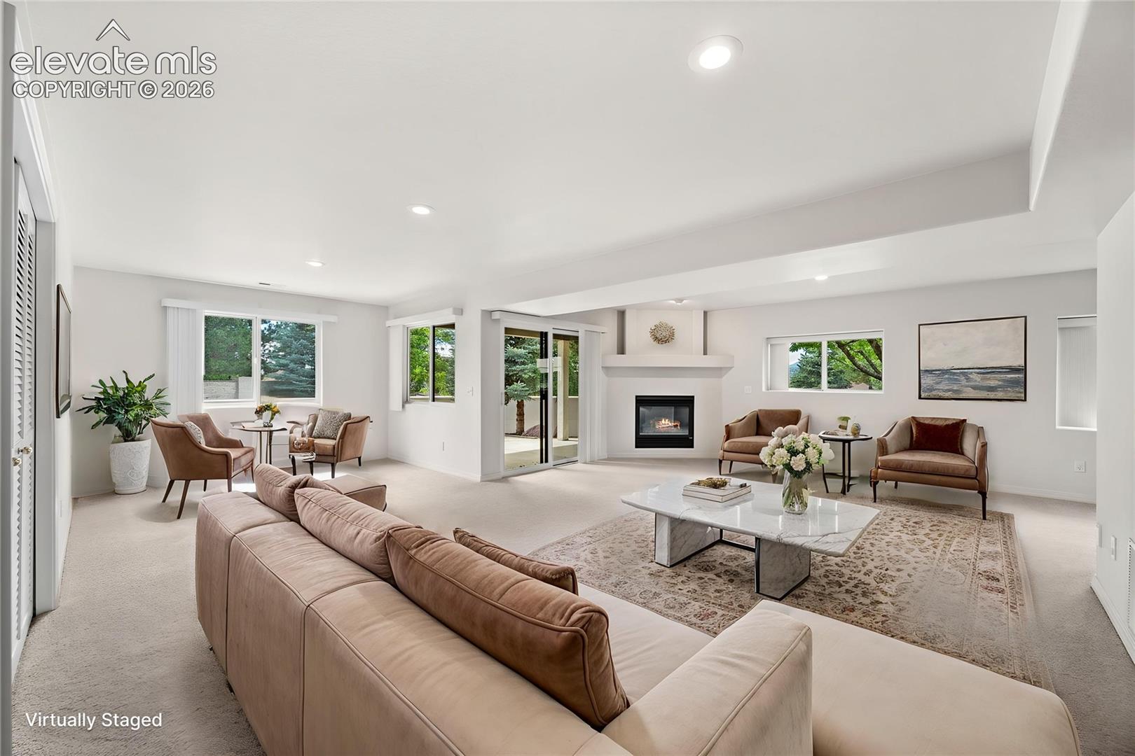 Open-concept interior featuring recessed lighting, a corner fireplace with a minimalist mantel, neutral carpeting, and sliding glass doors