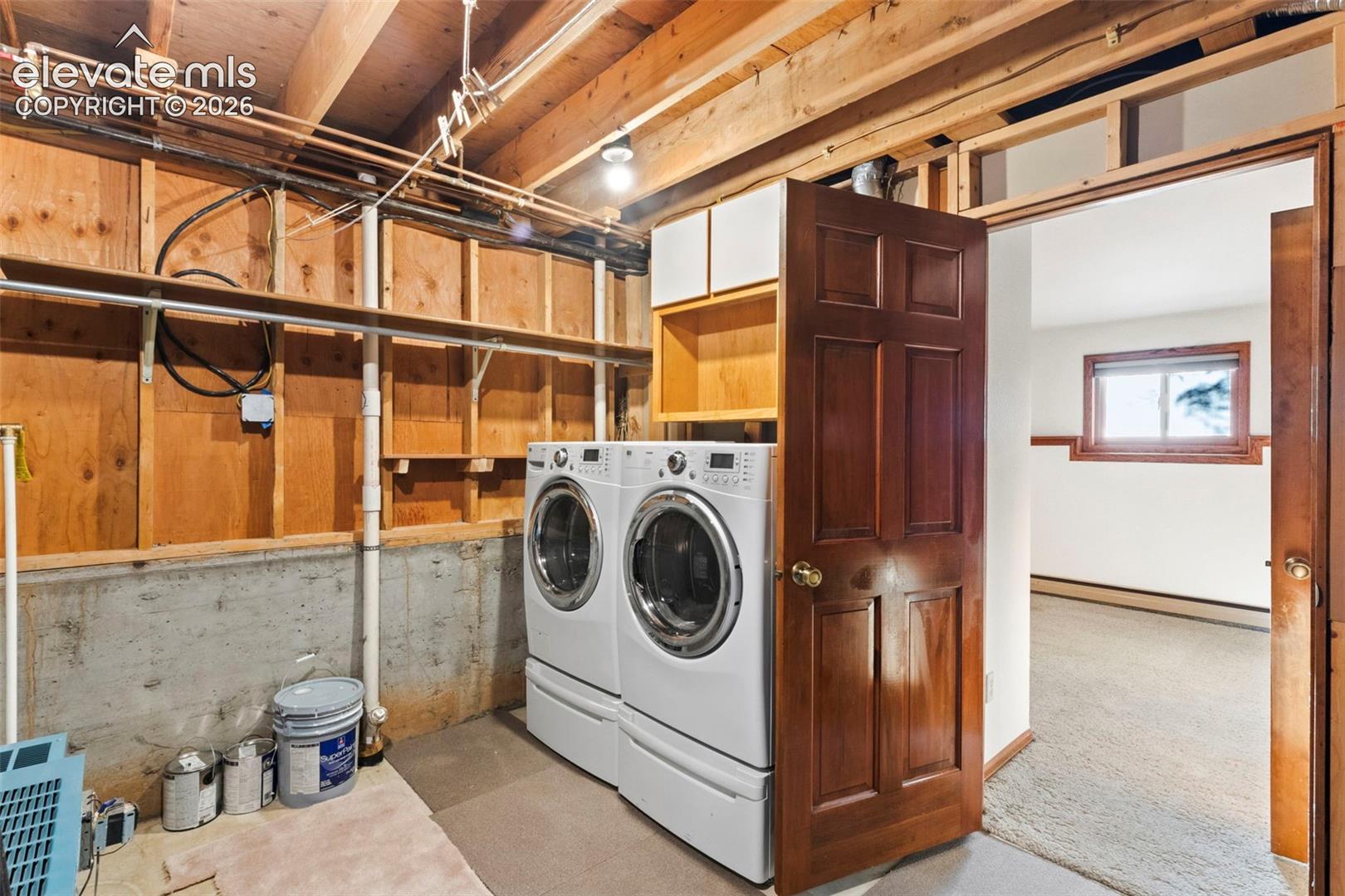 Utility area featuring exposed wood framing, concrete foundation walls, built-in shelving, and a six-panel wood door
