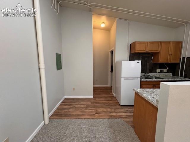 Kitchen featuring wood cabinetry, stone-patterned laminate countertops, and wood-finish flooring