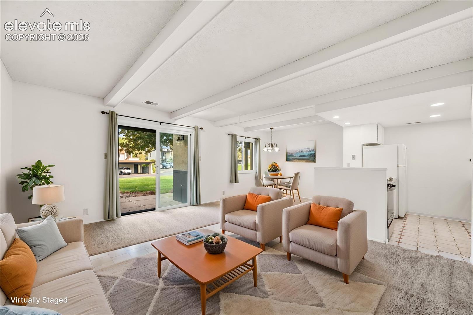 Open-concept interior featuring vaulted ceilings with exposed beams, sliding glass doors providing outdoor access, recessed lighting, and tile flooring in the kitchen area