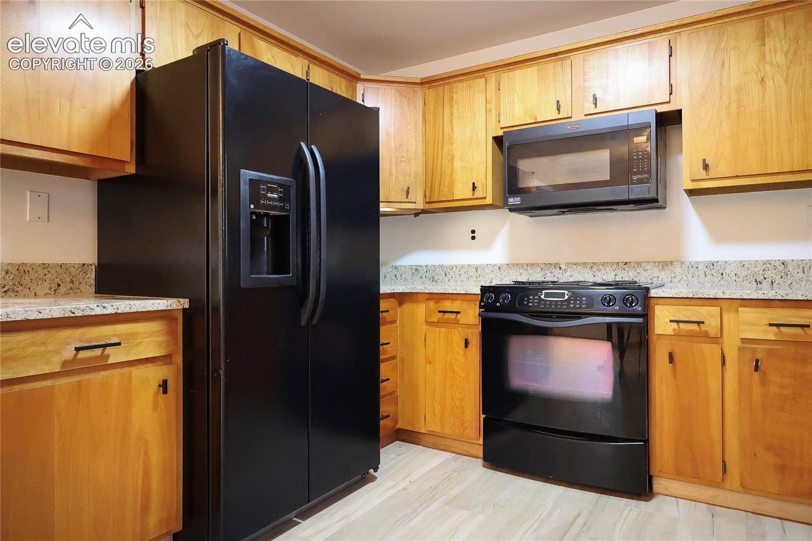 Kitchen featuring wood cabinetry, black appliances, light-toned countertops, and wood-finish flooring