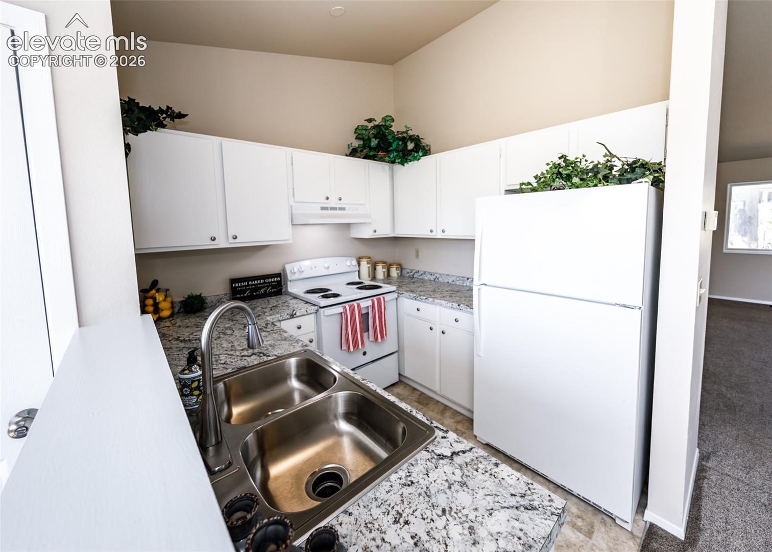 Kitchen featuring white cabinetry, a double basin stainless steel sink, a stainless steel faucet, and speckled countertops