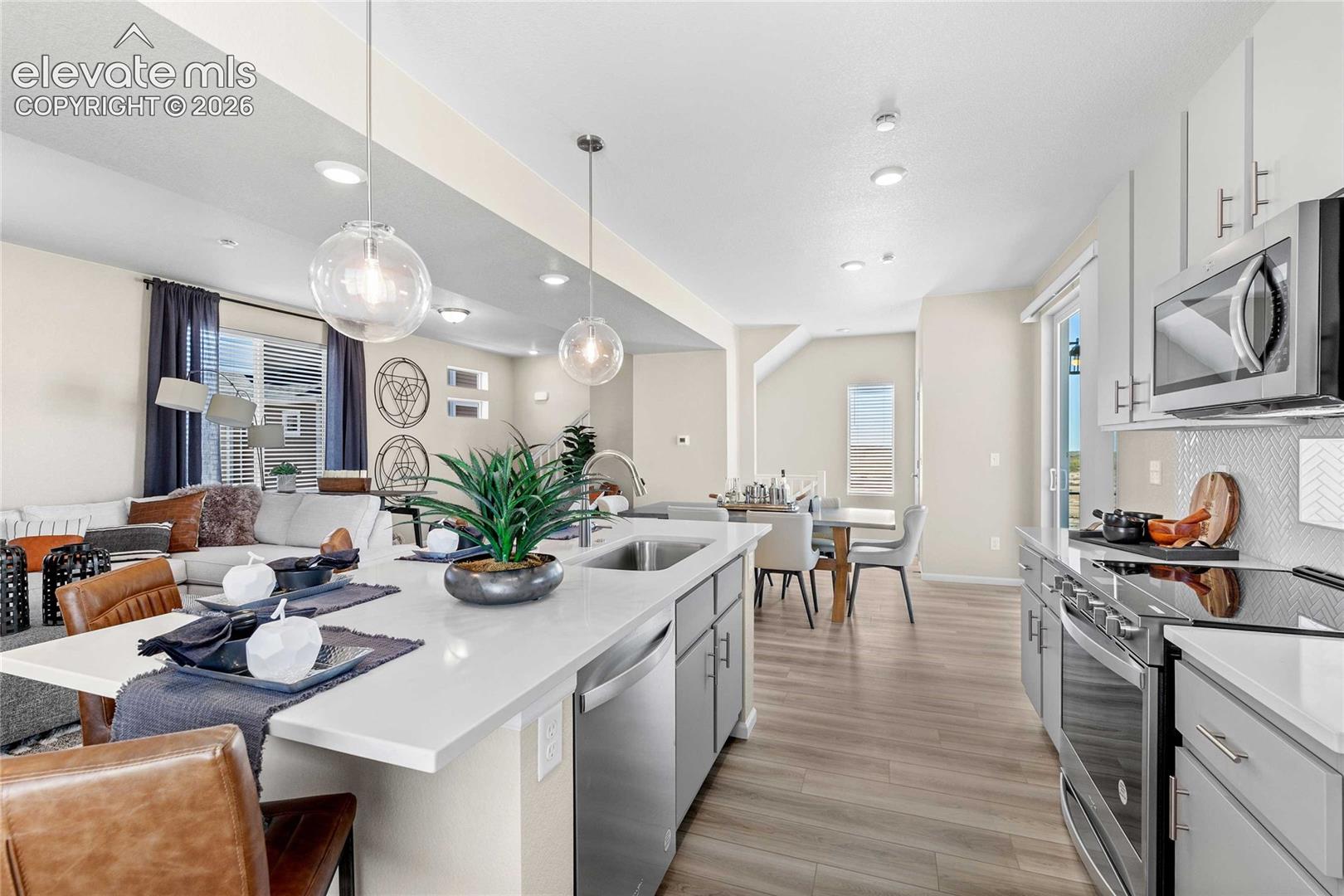 Open-concept living space featuring a kitchen island with seating, stainless steel appliances, pendant lighting, wood-finish flooring, and a sliding glass door
*photos of a model home*