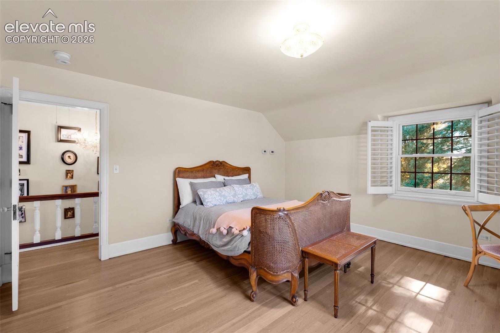 Bedroom featuring wood-finish flooring, multi-pane window with louvered shutters, and ceiling-mounted light fixture