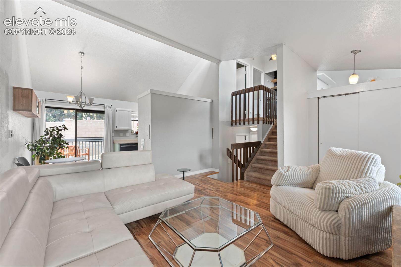 Vaulted ceiling, wood-finish flooring, staircase with wooden railing, built-in shelving, and sliding closet doors