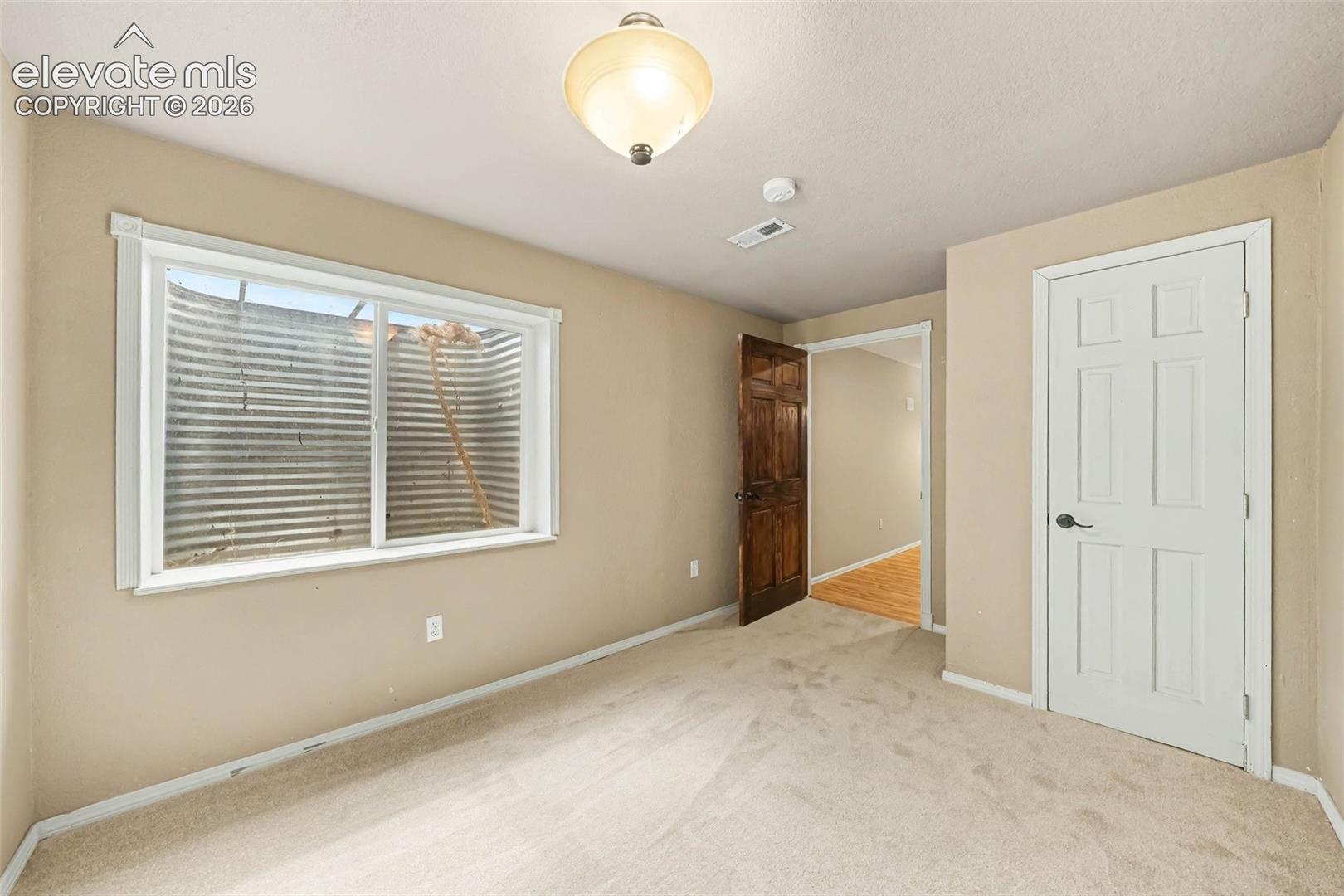 Carpeted flooring, egress window, paneled door, ceiling-mounted light fixture, and neutral wall tones