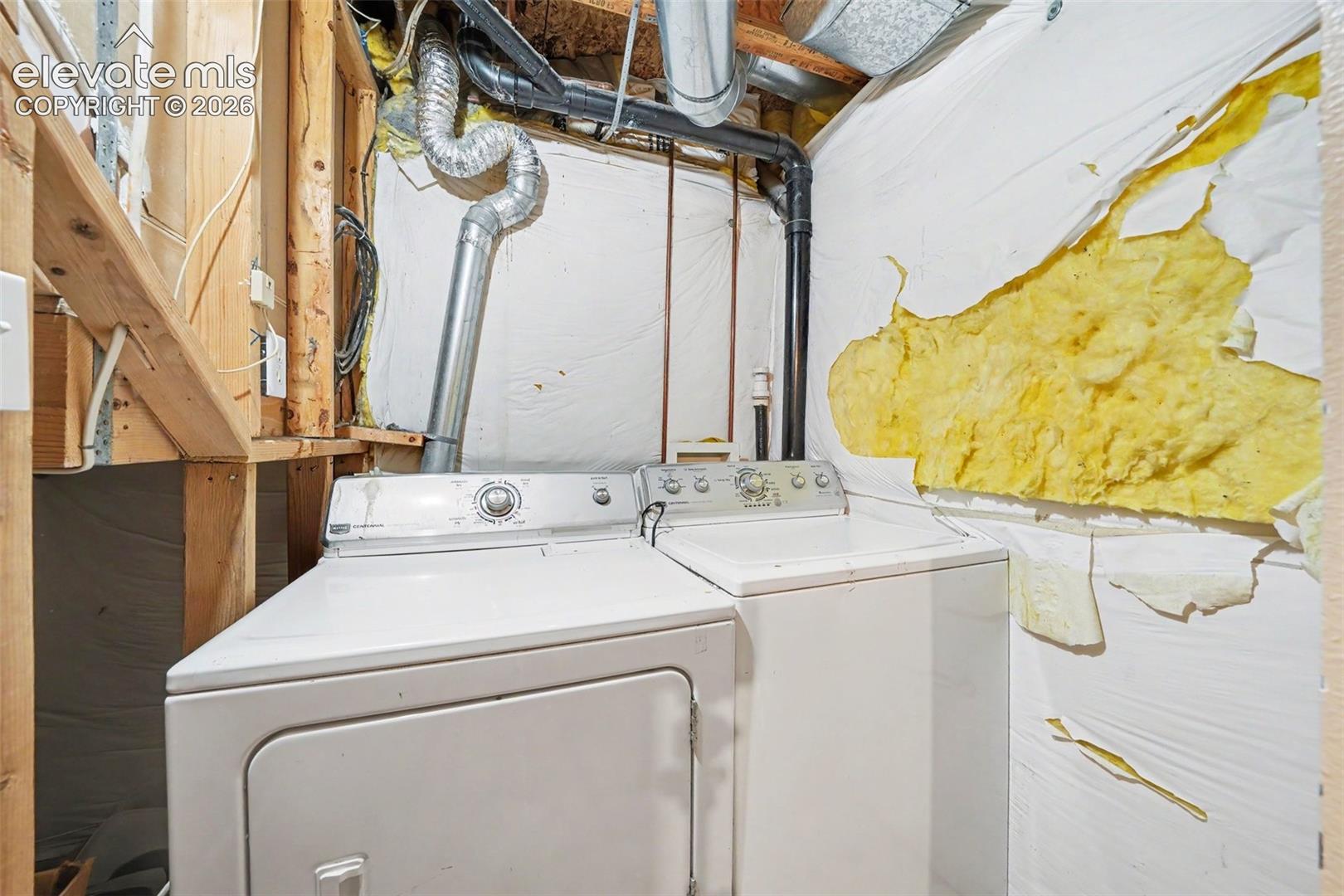 Utility area featuring white washing machine and matching electric dryer with exposed framing and insulated wall vapor barrier