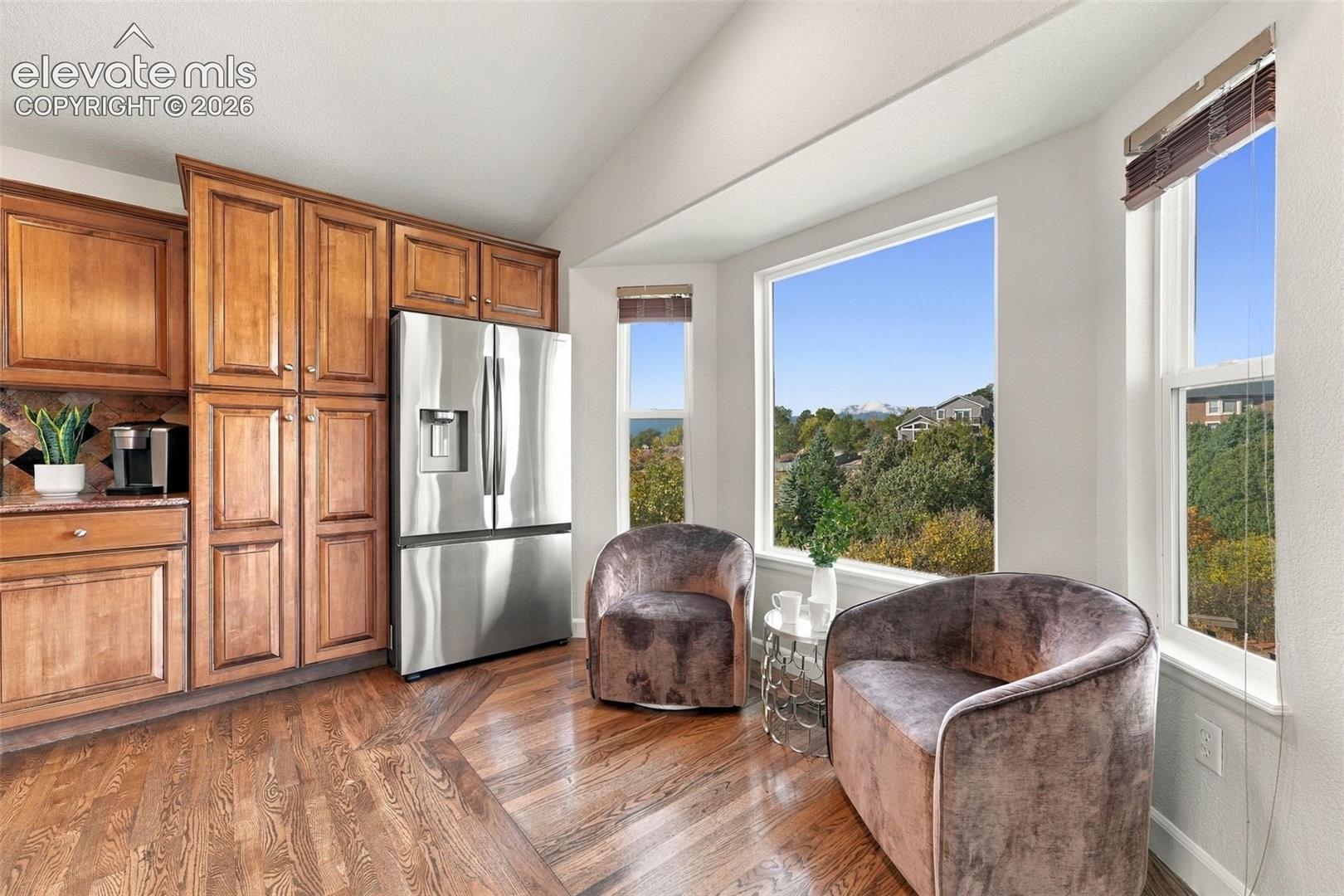 Kitchen featuring wood cabinetry, stainless steel refrigerator, wood-finish flooring, and a bay window configuration showcasing mountainous terrain