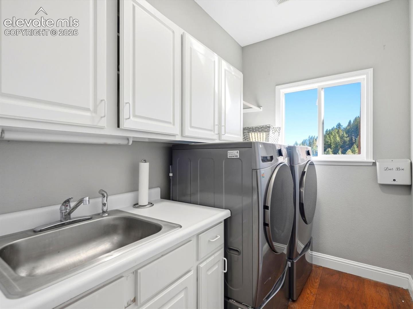Laundry room featuring white cabinetry, a stainless steel sink with a chrome faucet, wood-finish flooring, and a window with a mountain backdrop