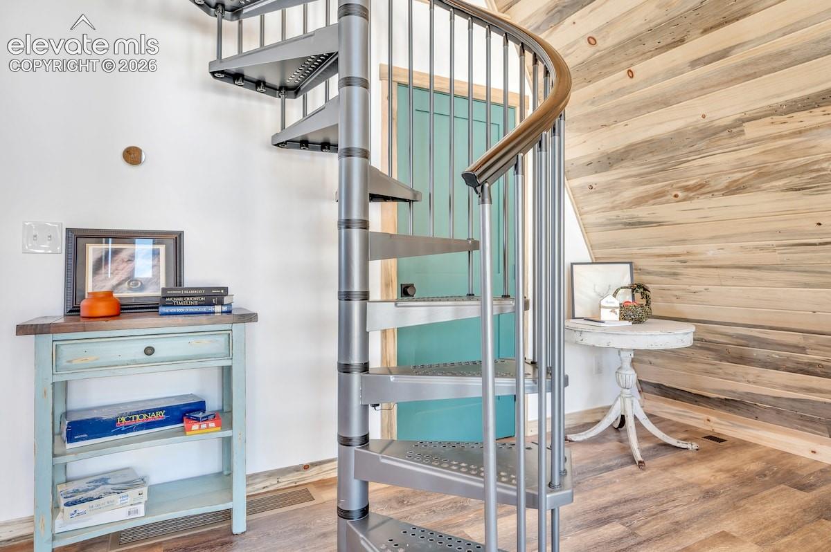 Spiral staircase featuring metallic construction, vertical balusters, and a curved wood handrail, accented by horizontal wood-plank wall paneling and wood-finish flooring