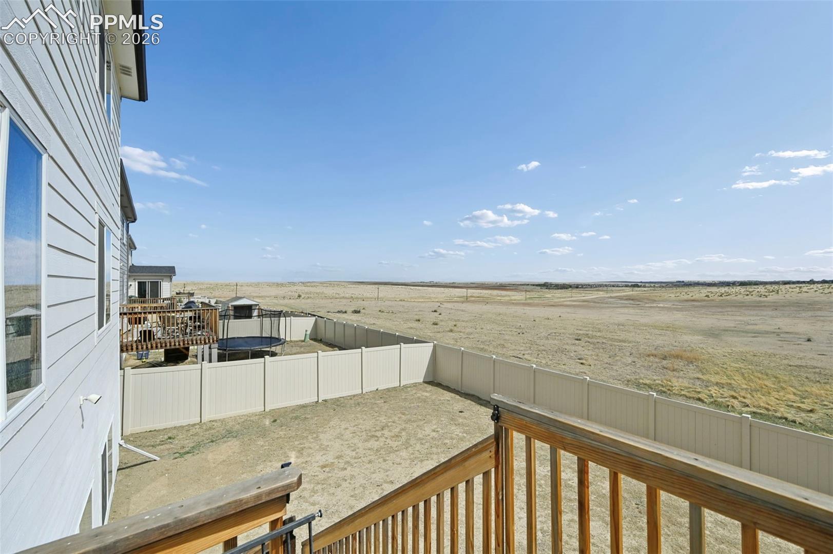 Expansive outdoor space featuring a white privacy fence, multi-level wood deck, and vast open fields beyond the property line