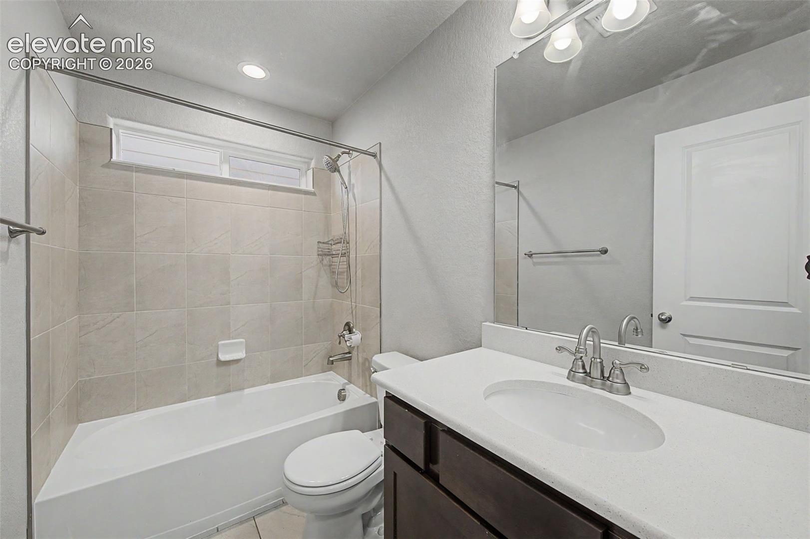 Bathroom featuring a white bathtub, tiled shower surround, horizontal transom window, dark wood-finish vanity with white countertop, and a large mirror
