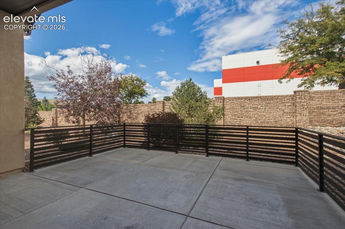 Concrete patio enclosed by horizontal metal fencing with a stone-textured perimeter wall and established landscaping