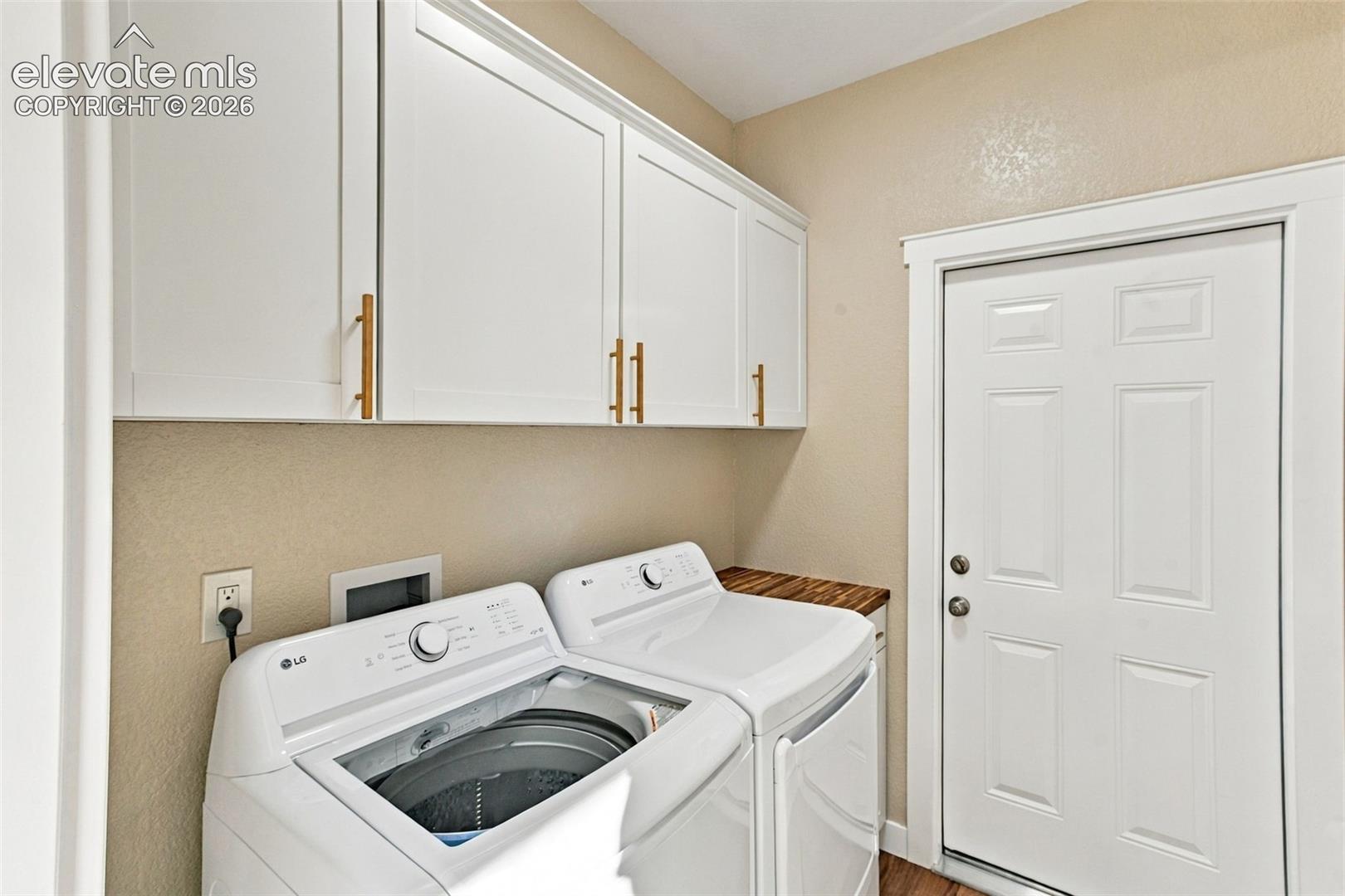 Wall-mounted shaker-style cabinetry with metallic hardware, wood-finish countertop, and a six-panel door