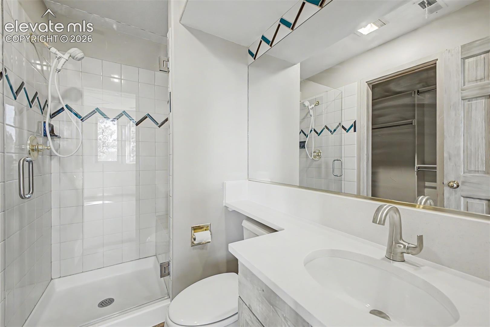 Glass-enclosed shower with tile surround, vanity with integrated sink, and full-width wall mirror
