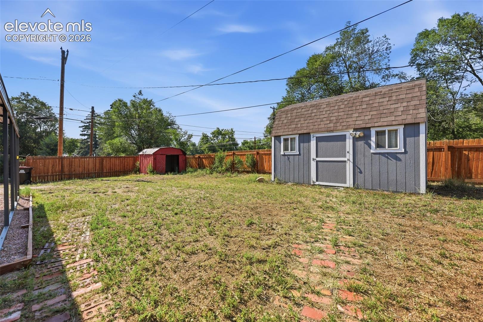 Spacious backyard featuring a utility shed with a shingle roof and two windows, a second storage shed, and wood fencing.
