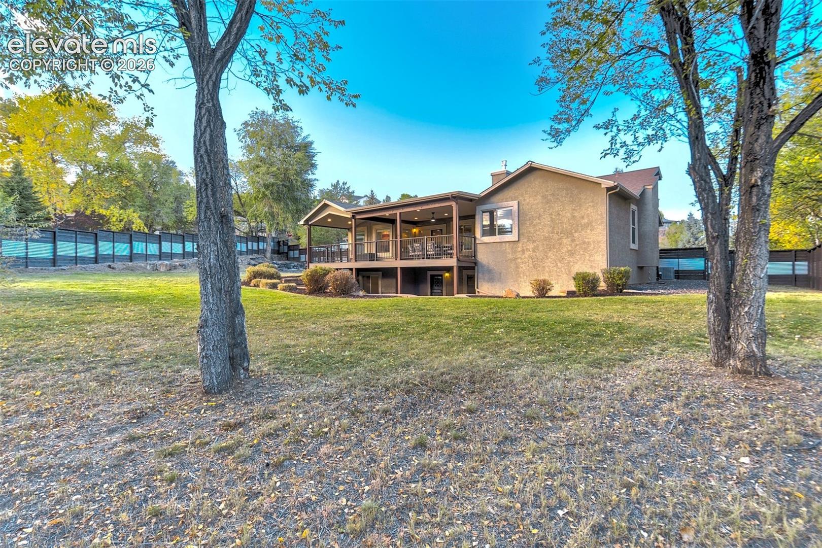 Expansive backyard featuring a large grass lawn, mature trees, and a covered deck with railing