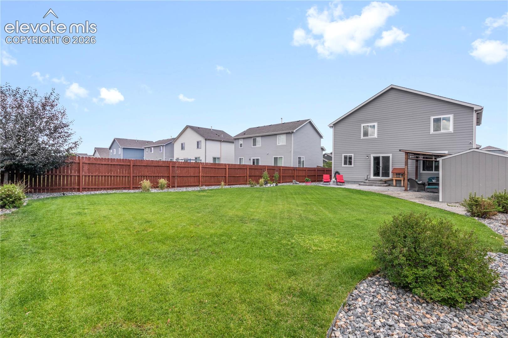 Expansive green lawn with a brown privacy fence, complemented by a patio area and a detached storage shed