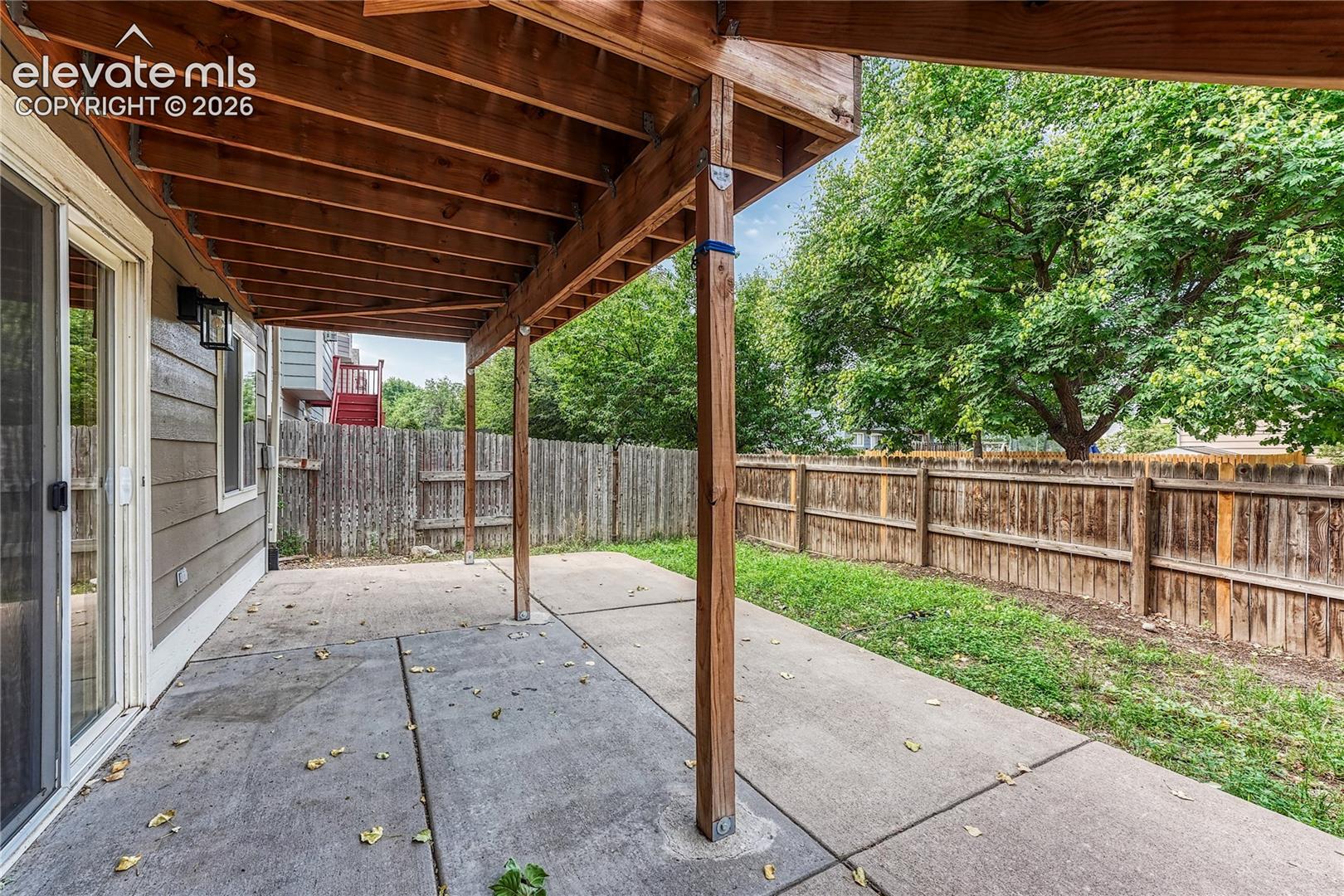 Covered concrete patio with wood framing, sliding glass door entry, and perimeter wood privacy fencing