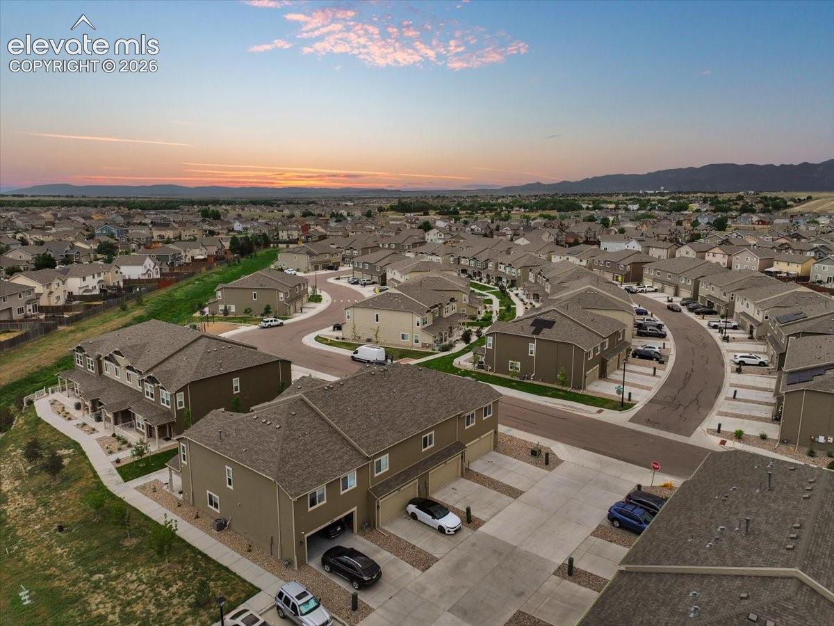 Residential neighborhood featuring a series of multi-story homes with attached garages, paved streets, and a distant mountain range