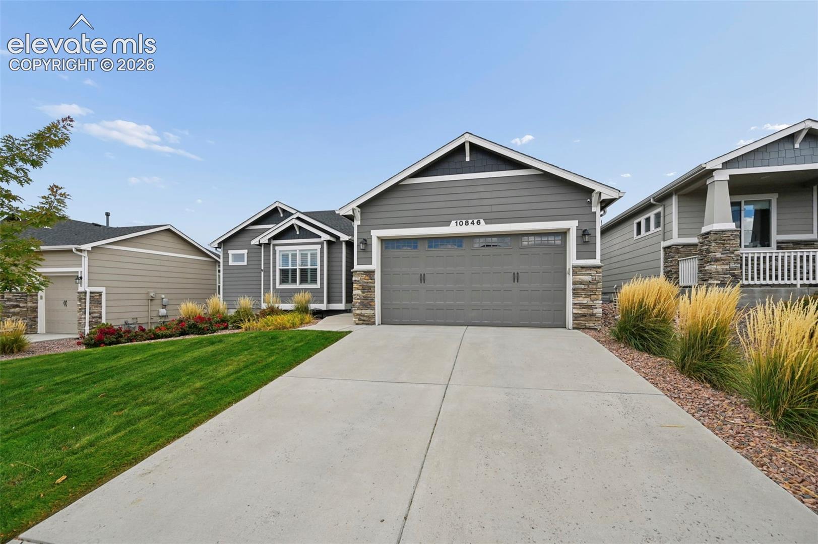 Exterior featuring horizontal lap siding, stone veneer accents, a multi-car garage, concrete driveway, and manicured lawn