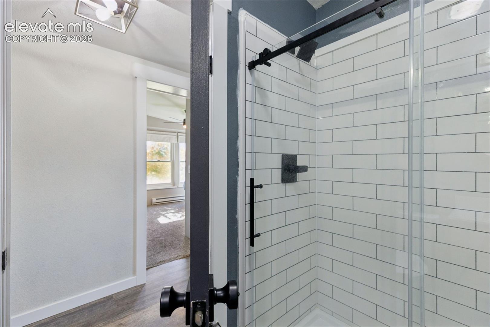 Shower enclosure with white subway tile surround, matte black hardware, and a glass sliding door featuring a black track system