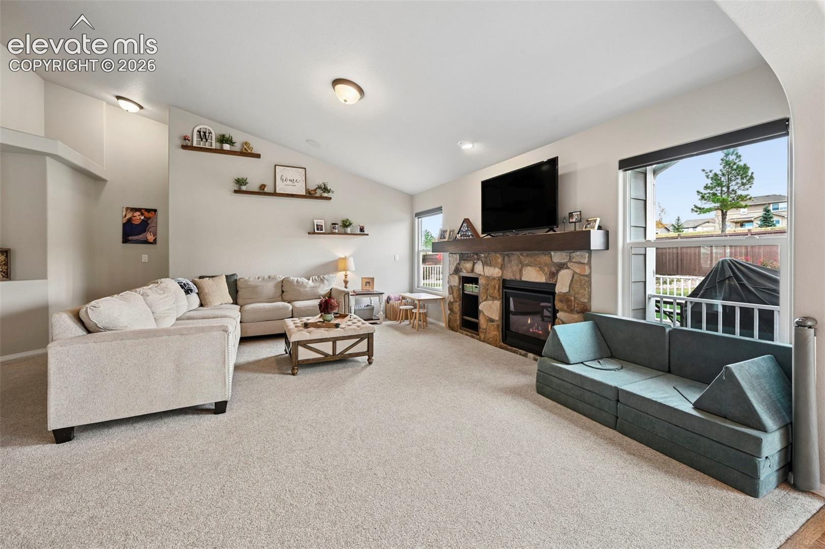 Vaulted ceilings, stone-faced fireplace with a wood mantel, recessed lighting, and wall-mounted shelving