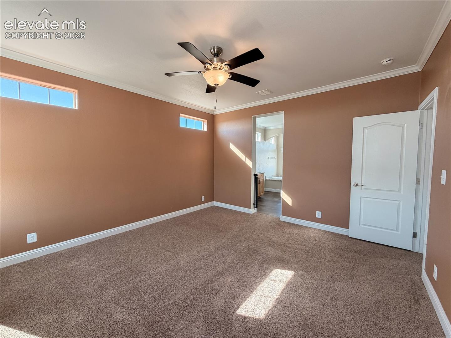 Room featuring high ceilings with crown molding, carpeting, a ceiling fan with integrated lighting, clerestory windows, and a solid-core panel door