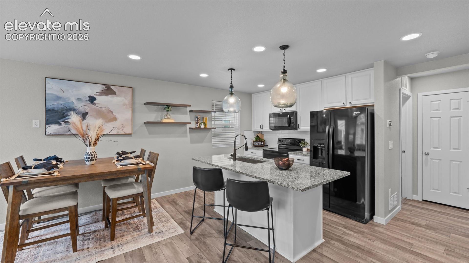 Kitchen featuring white cabinetry, stone-surface island with an integrated sink, matte black plumbing fixtures, wood-finish flooring, and recessed lighting
