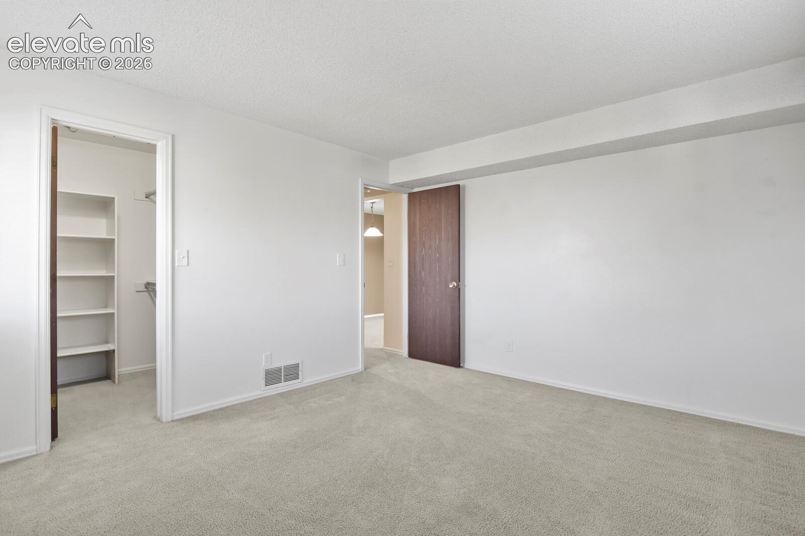Another view of the bedroom towards the door. Neutral wall-to-wall carpeting, walk-in closet featuring built-in shelving