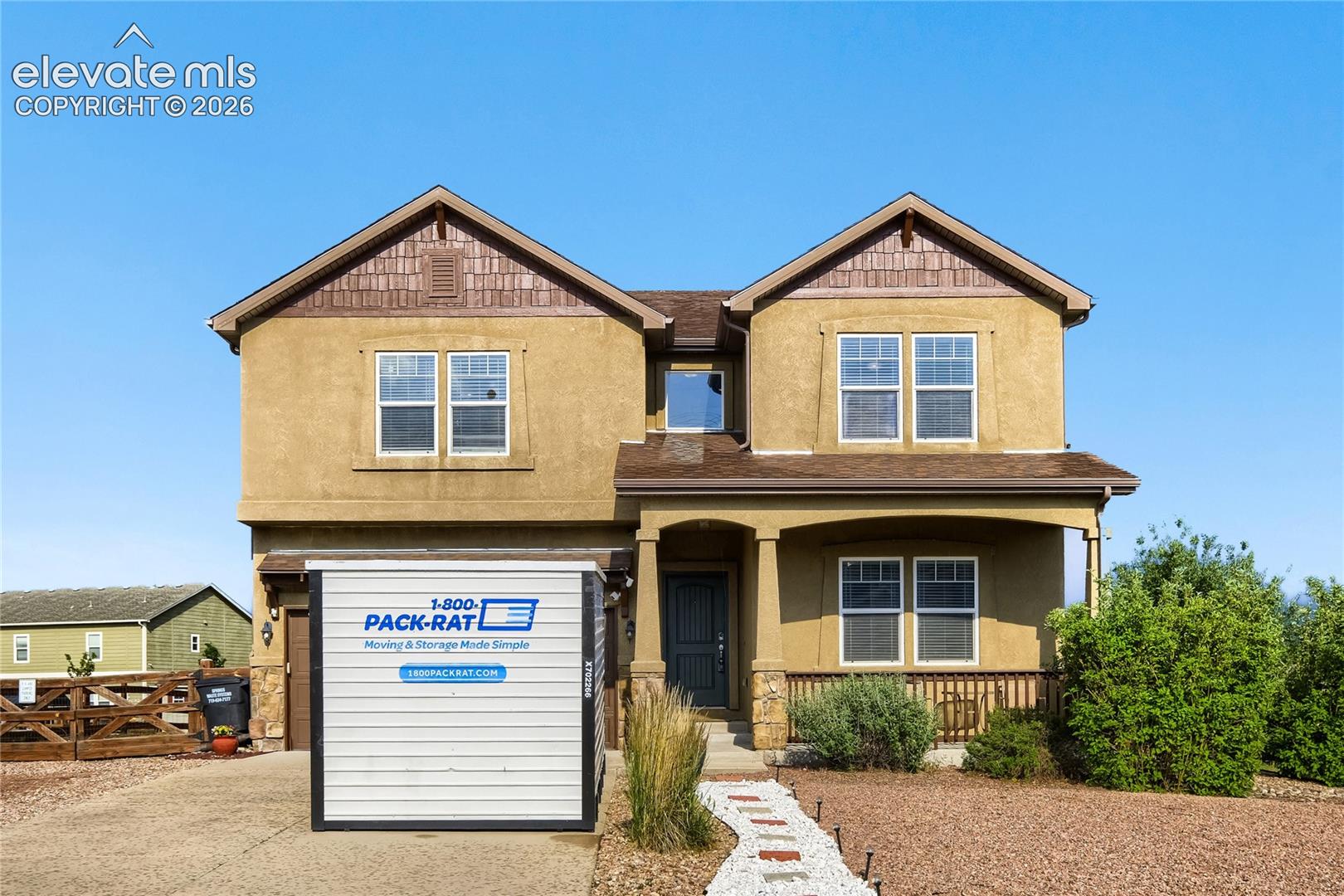 Two-story stucco property featuring a covered front porch with stone-wrapped columns