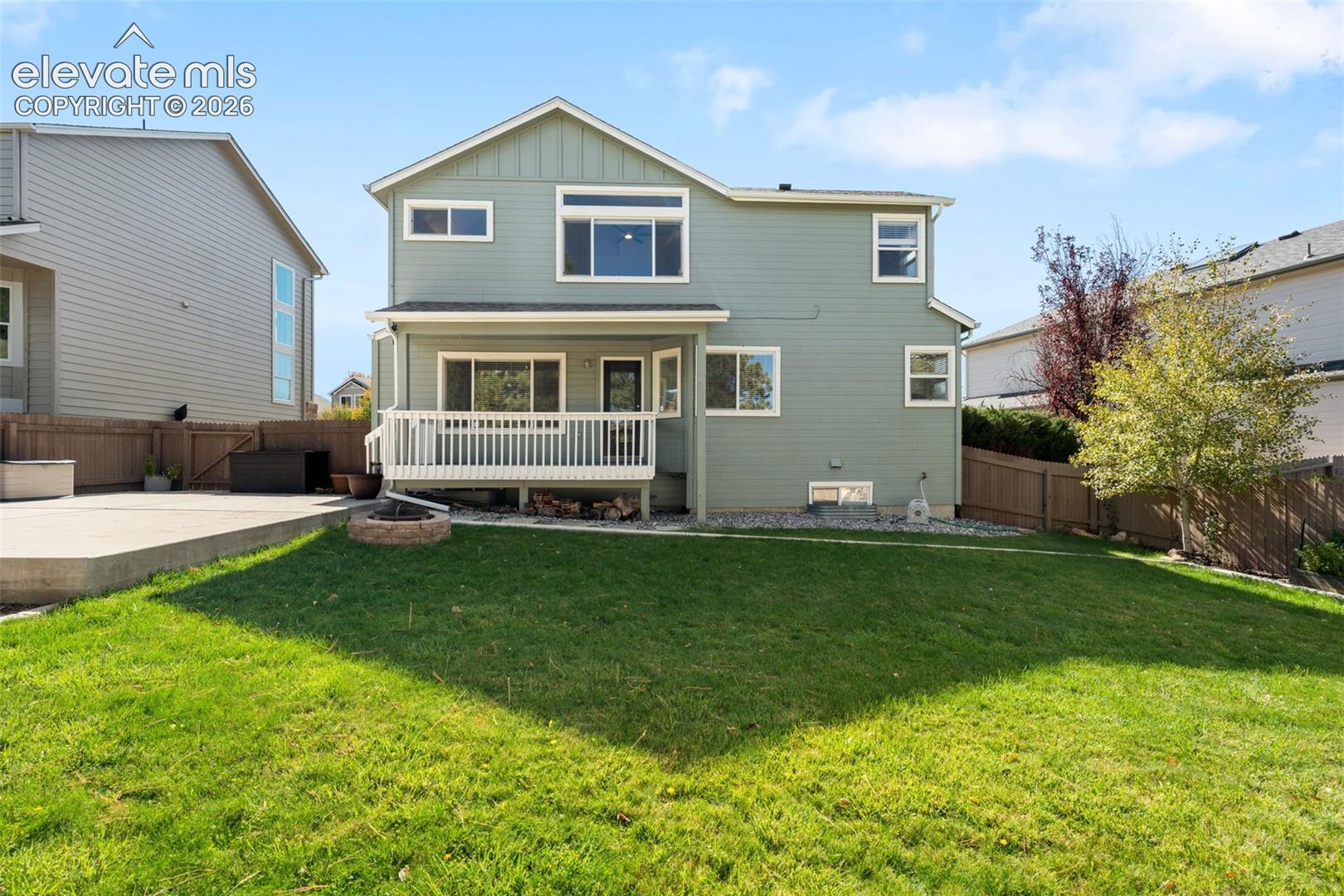 Two-story exterior featuring horizontal siding, a raised rear deck with balustrades, concrete hardscaping, a stone fire pit, and enclosed wood fencing