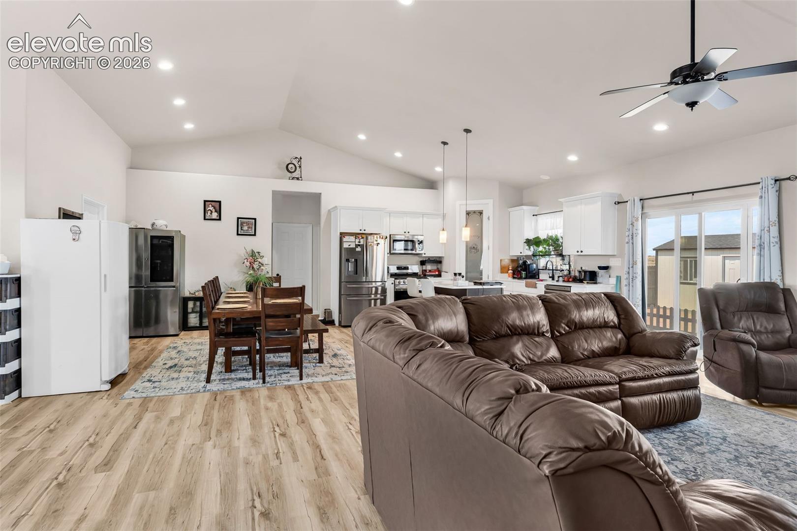 Open-concept living area featuring vaulted ceilings with recessed lighting, wood-finish flooring, a ceiling fan, and a kitchen with white cabinetry