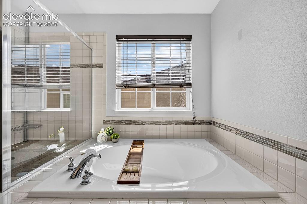 Integrated soaking tub with chrome fixtures, tiled surround, and decorative mosaic accent strip