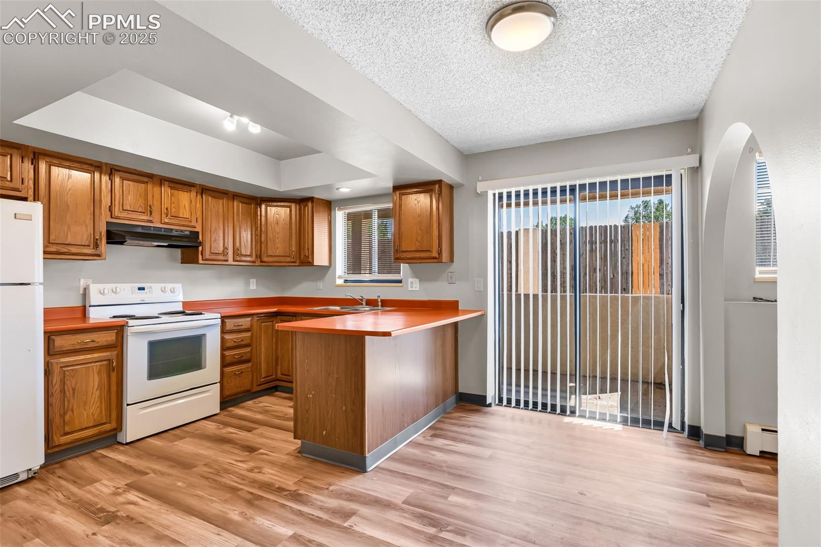 Kitchen featuring brown cabinets, white appliances, light wood-type flooring, a peninsula, and light countertops