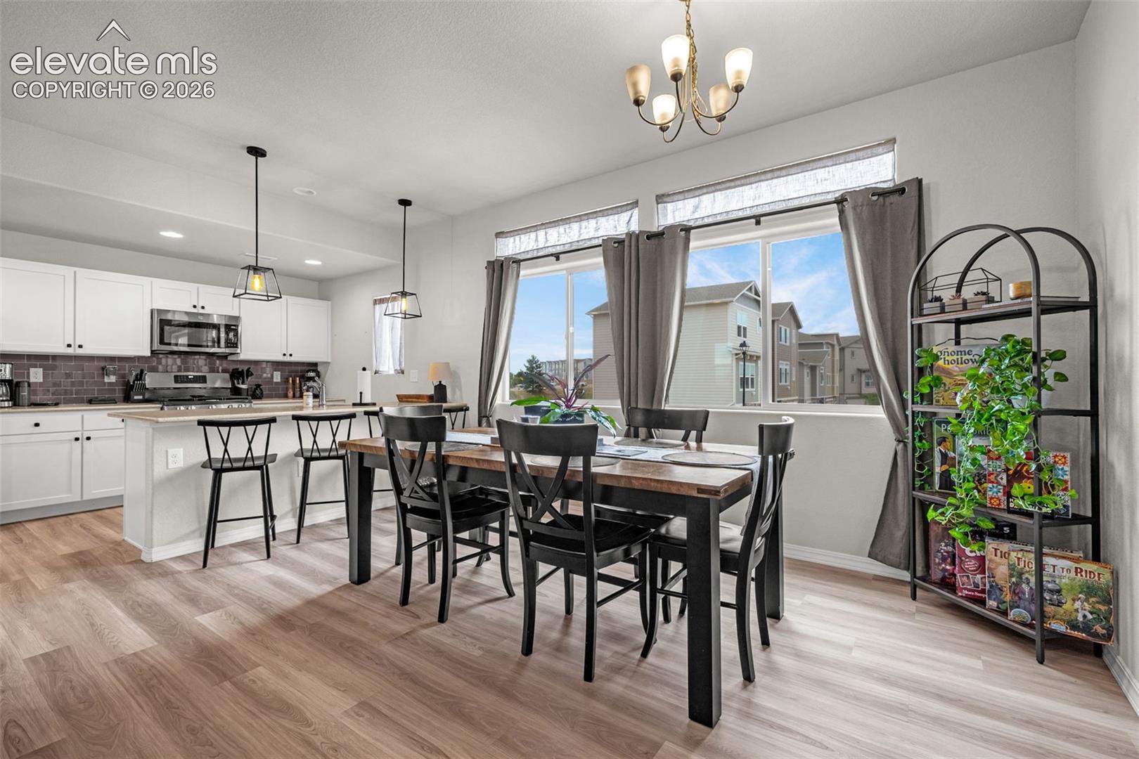 Open-concept kitchen and dining area featuring white cabinetry, a kitchen island with seating, stainless steel appliances, and wood-finish flooring