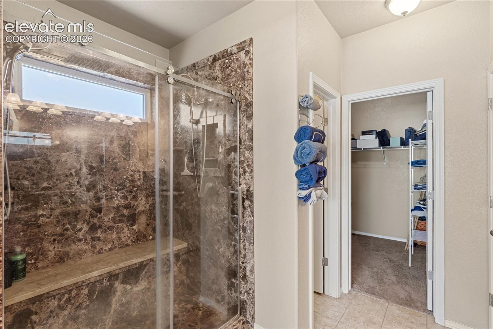Walk-in shower featuring a built-in stone bench, glass sliding enclosure, rainfall shower head, and stone wall surrounds with a horizontal transom window