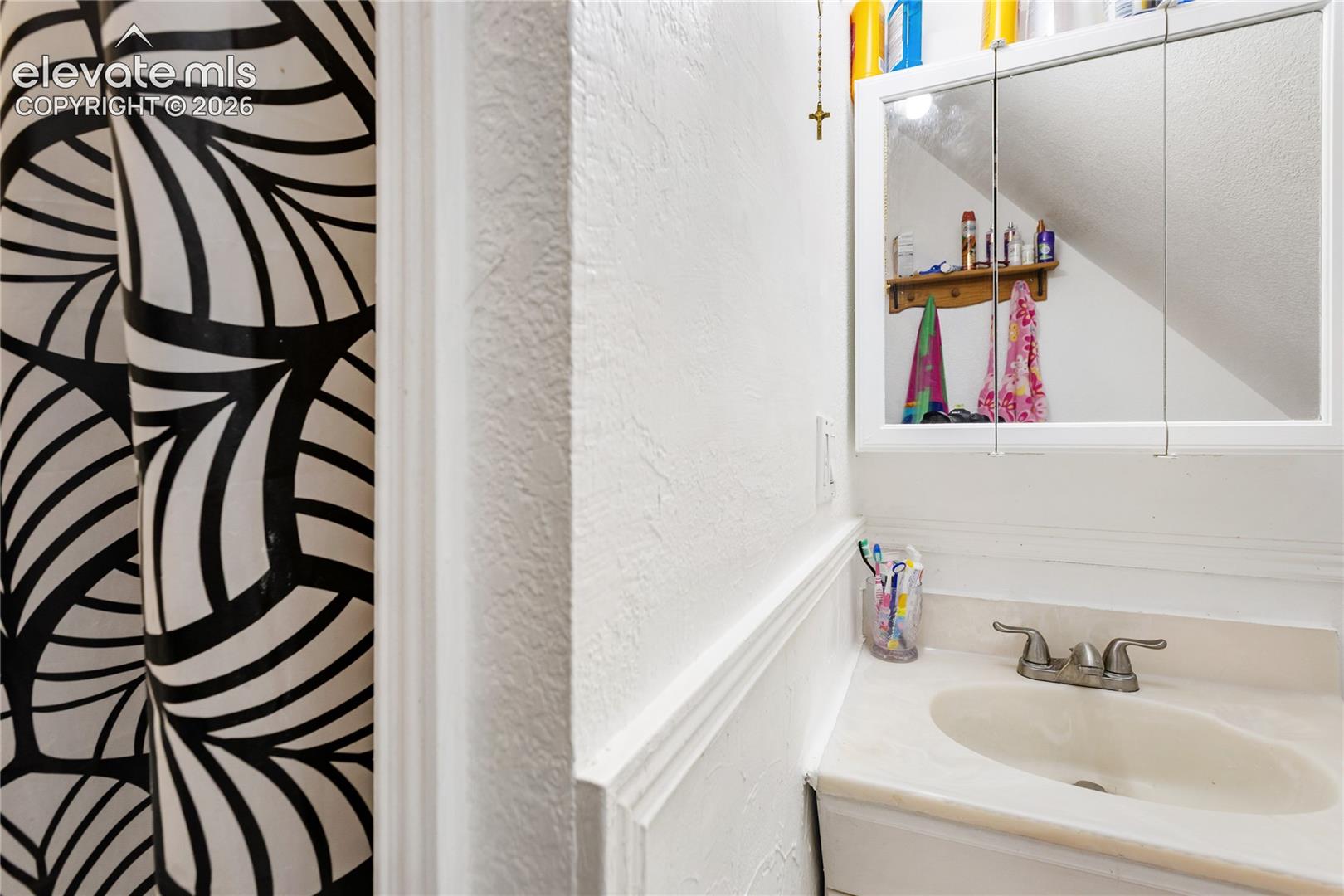 Bathroom vanity featuring a recessed sink, two-handle metal faucet, and integrated tri-fold mirrored medicine cabinet with built-in shelving