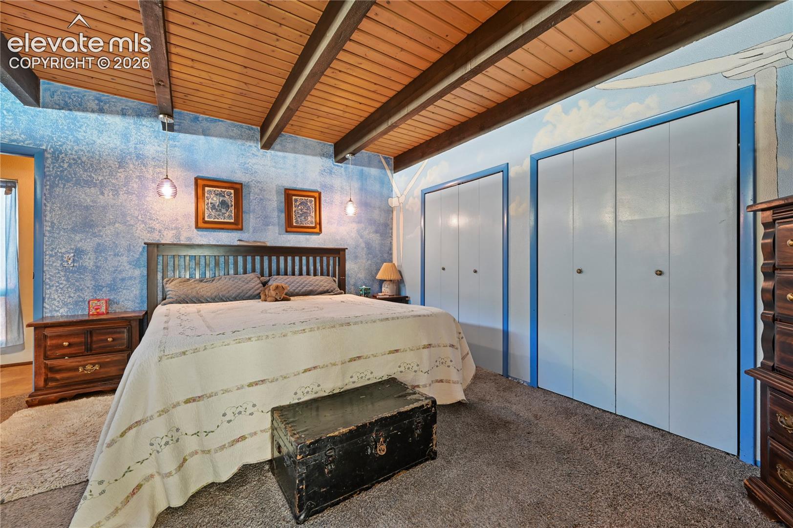 Main bedroom, Vaulted wood-paneled ceiling with exposed beams, textured accent wall, two sets of bi-fold closet doors, and wall-mounted pendant lighting