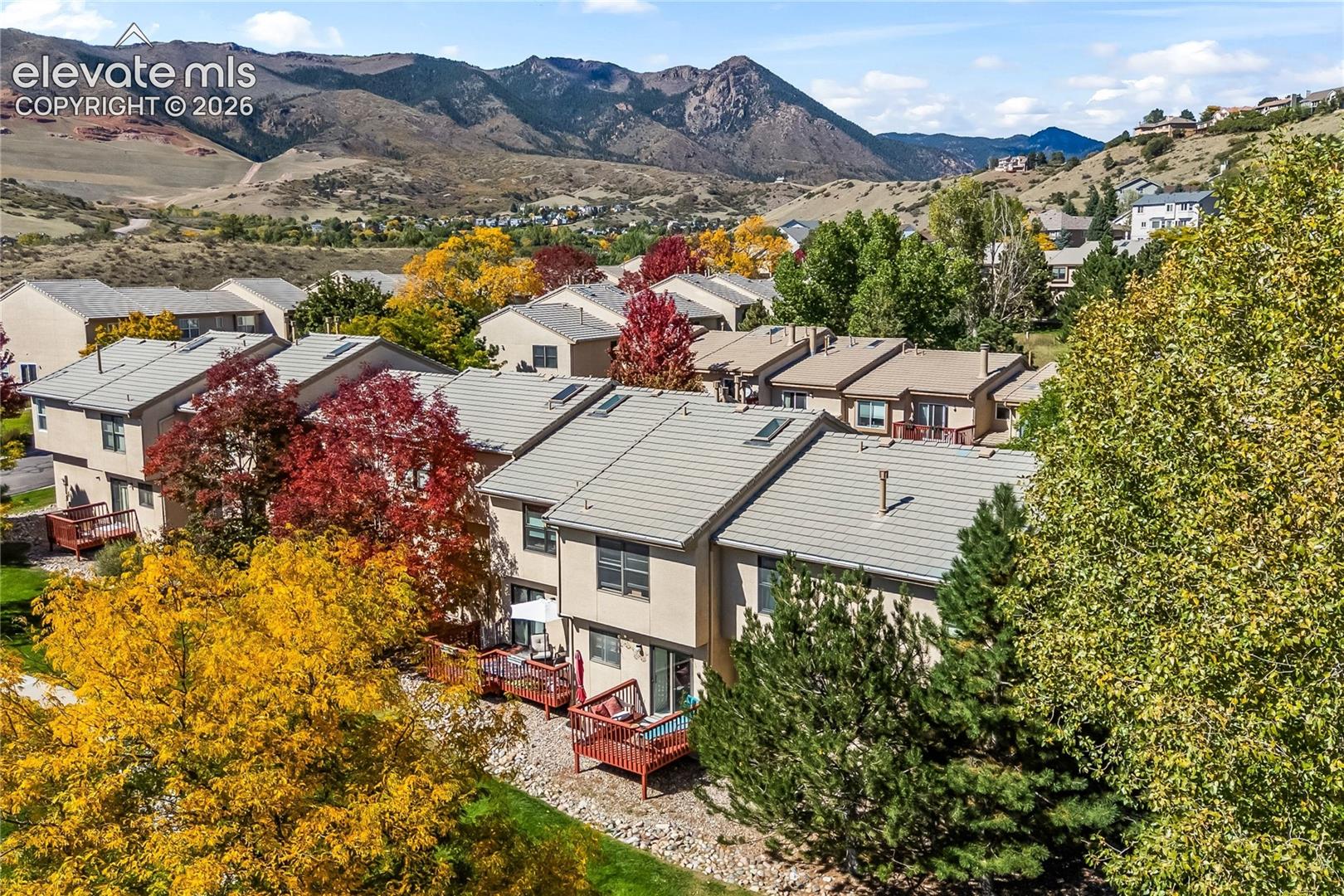 Mountain backdrop with multiple residential structures featuring light-colored siding, gray shingle roofs with skylights, and individual wooden decks