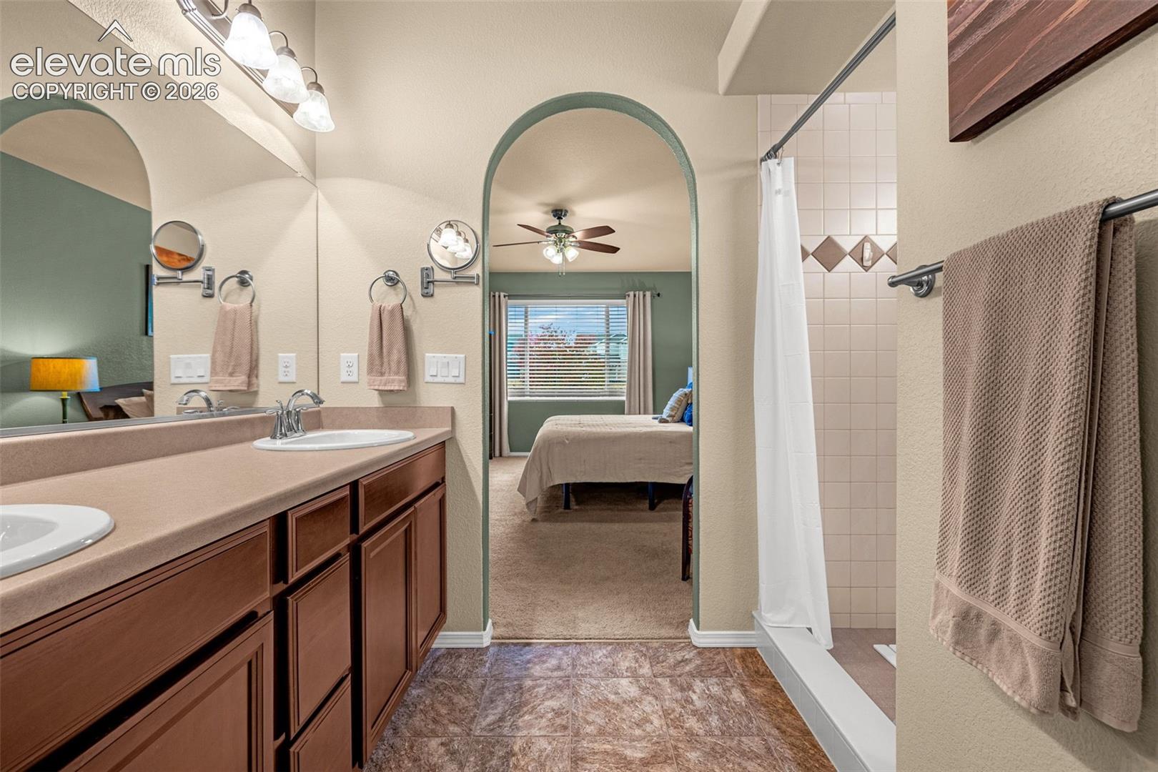 Bathroom featuring a double-sink vanity with a solid-surface countertop, archway architectural detail, and a tiled shower enclosure