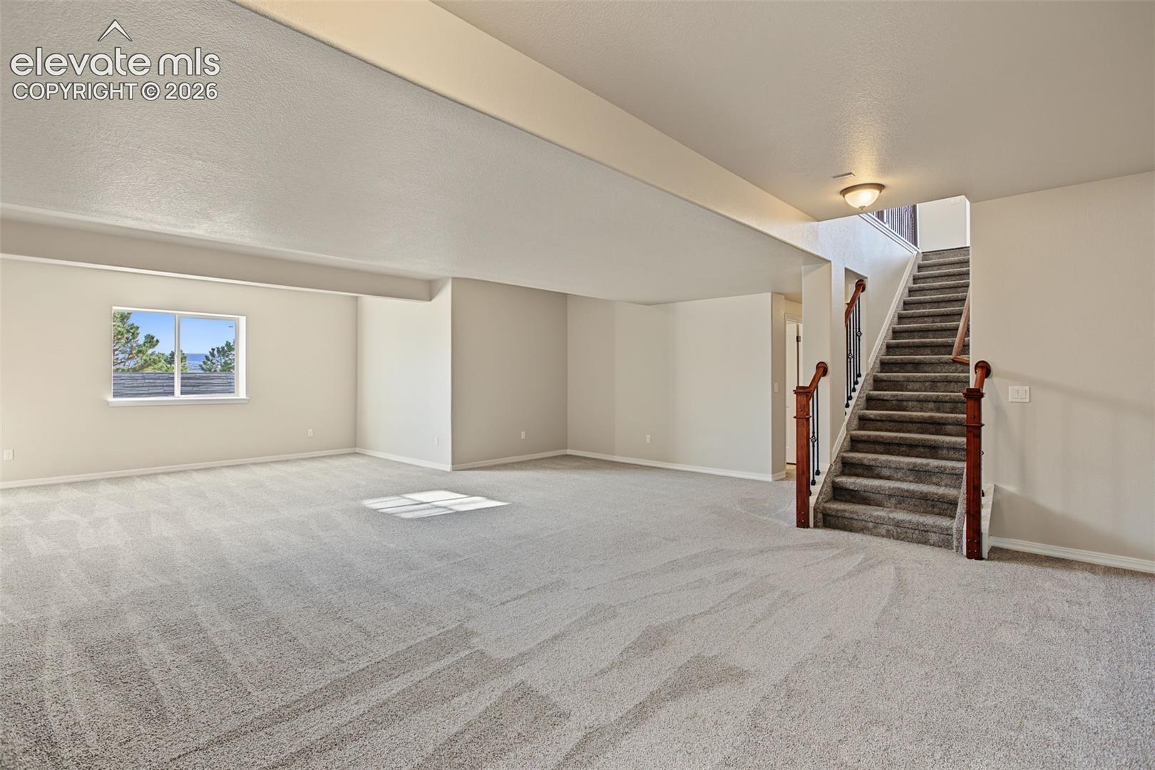 Open-concept interior featuring wall-to-wall carpeting, wood-finish handrails with metal balusters, and a single-pane window