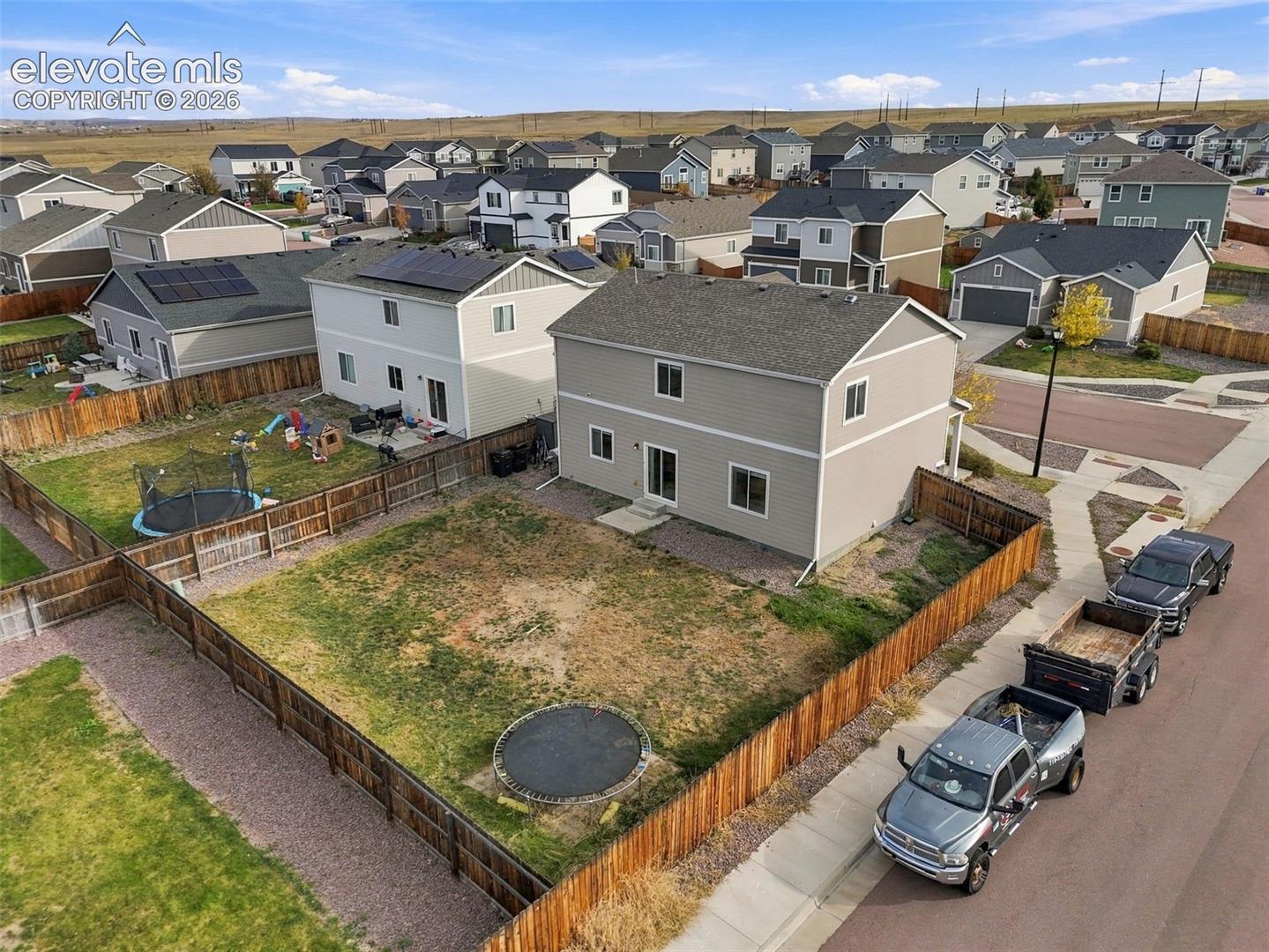 Two-story residence featuring light-toned horizontal siding, a gabled roof with integrated solar panels, a fenced rear yard, and a concrete patio