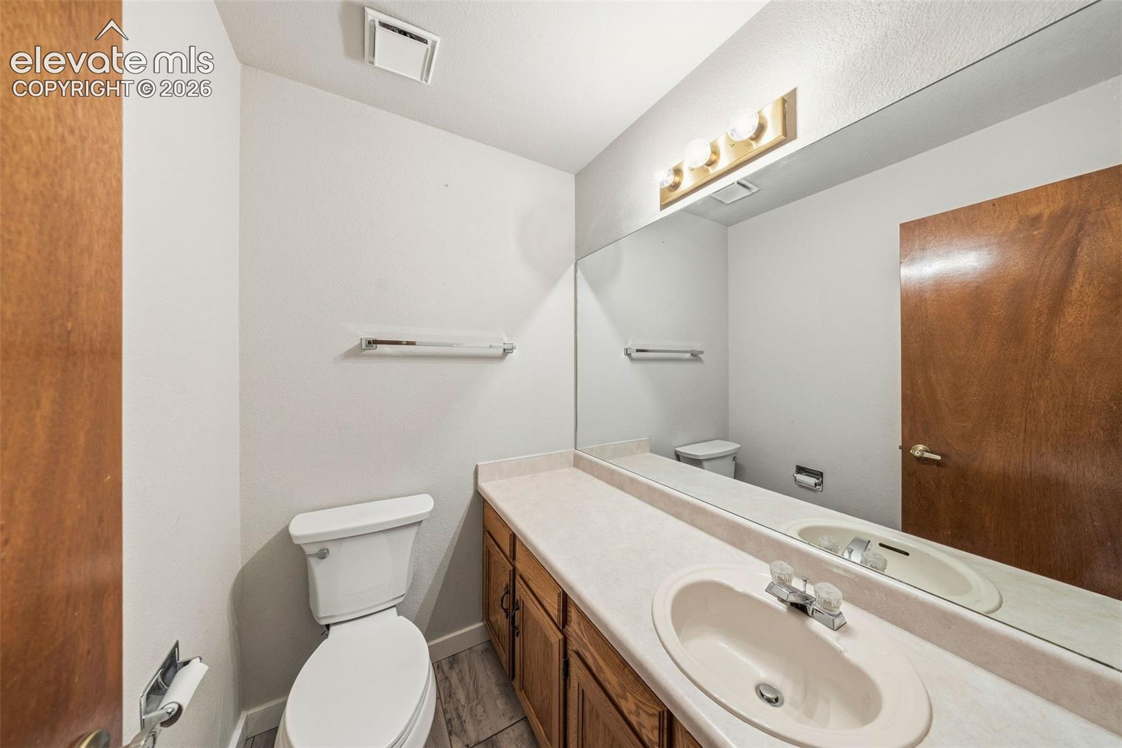 Bathroom featuring a single-sink vanity with wood-finish cabinetry, an integrated basin, a large wall-mounted mirror, and three-bulb vanity lighting