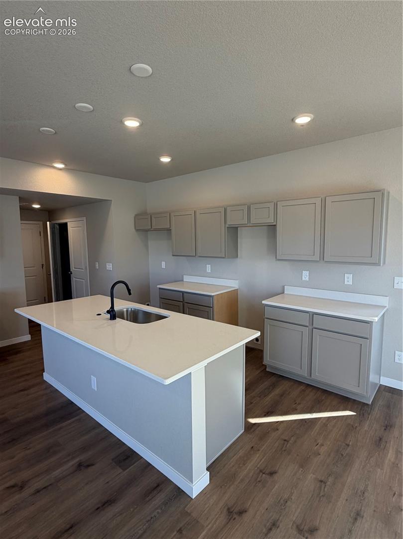 Kitchen featuring grey cabinetry, white countertops, a center island with an integrated sink and matte black faucet, and wood-finish flooring