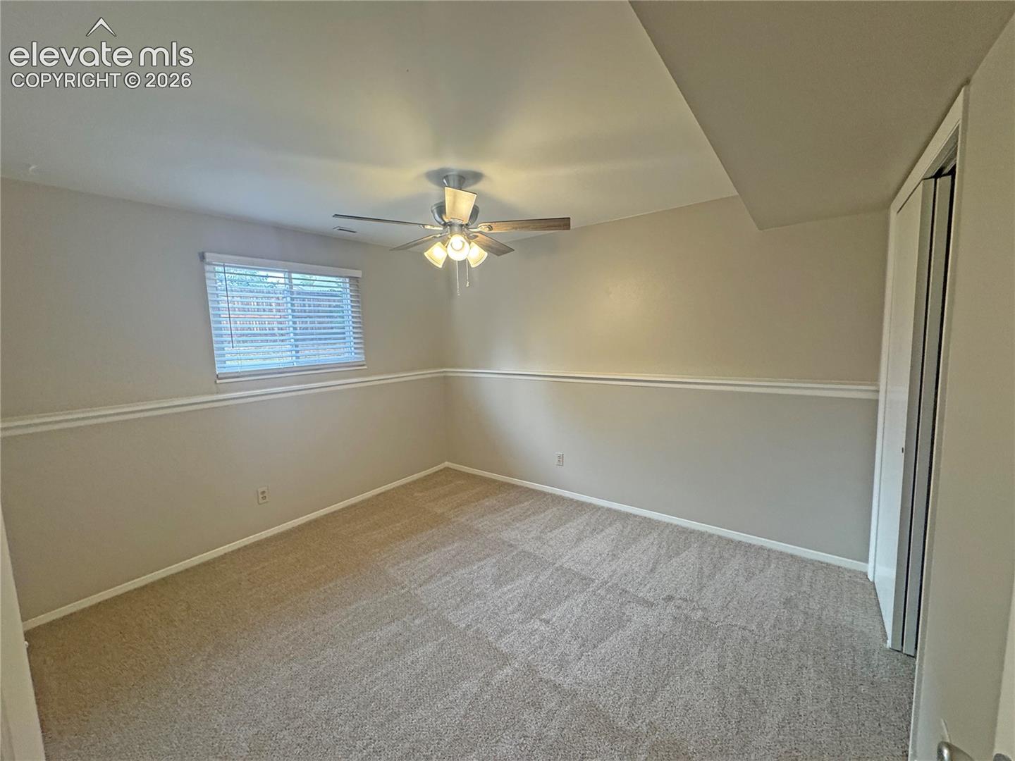 Neutral carpeting, chair rail molding, multi-blade ceiling fan with integrated lighting, and dual-panel sliding closet doors