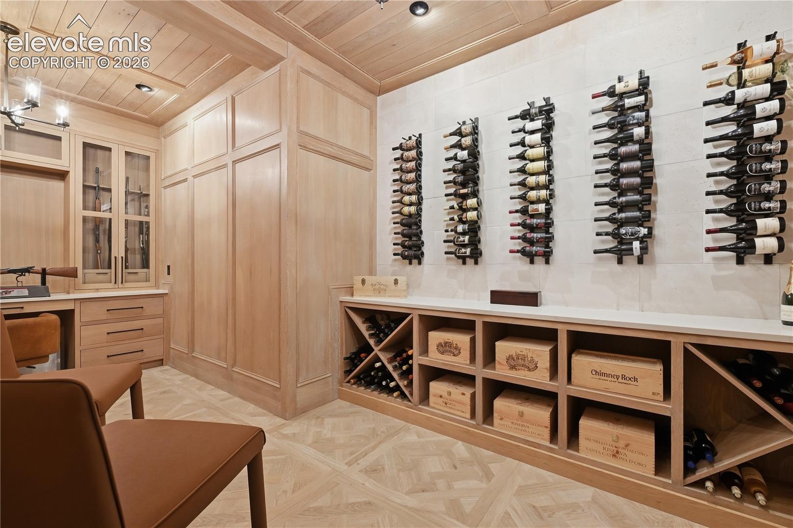 Custom wine cellar featuring extensive light wood millwork, coffered wood-paneled ceiling, stone wall cladding, built-in display cabinetry, and geometric floor patterning