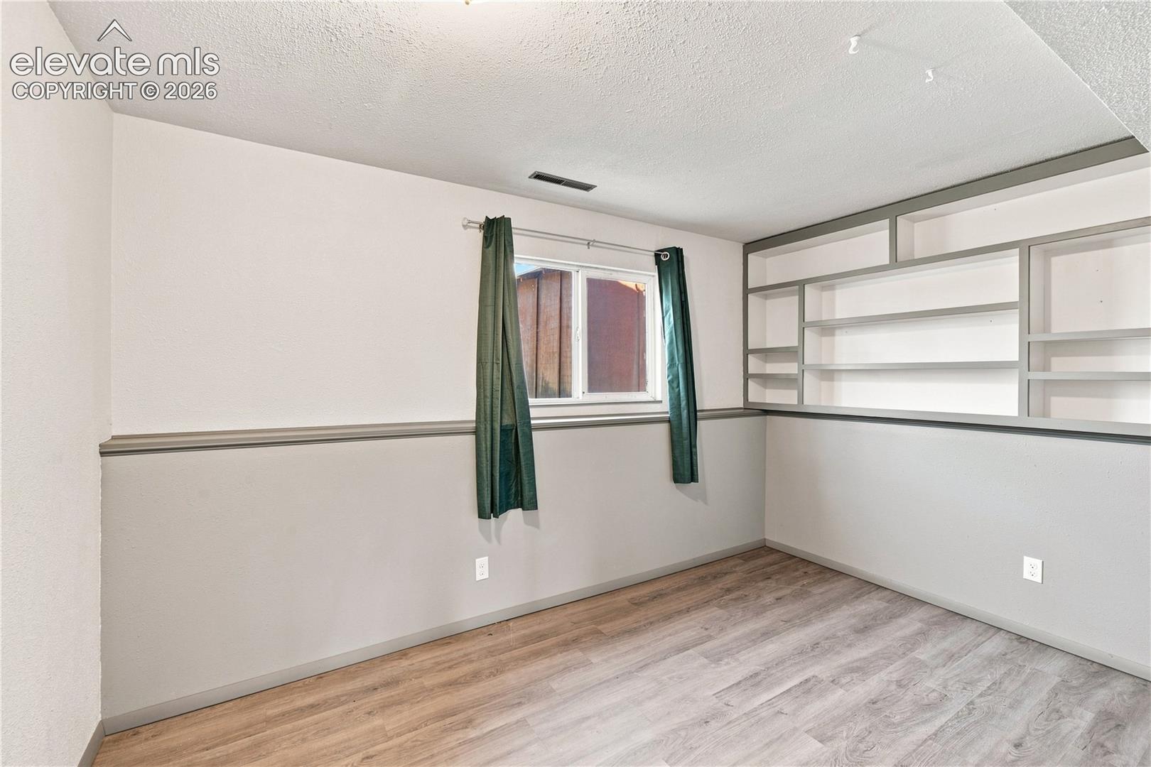 Wood-finish flooring with built-in shelving, a single window, and a white and grey painted wall